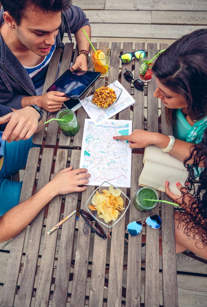 Friends sitting on bench with snacks checking maps