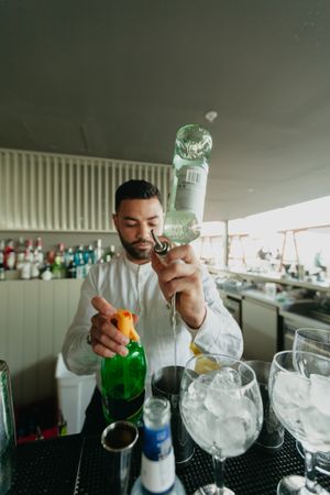 Barman pouring cocktail and alcoholic drinks to shaker in a bar.