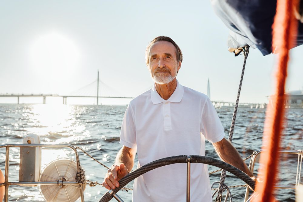 Older man at the helm of a boat with a bridge in the back