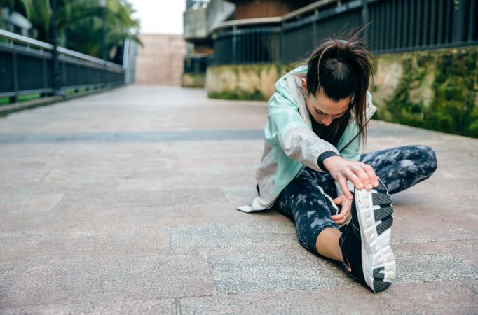 Woman runner looking down while stretching leg before training in town