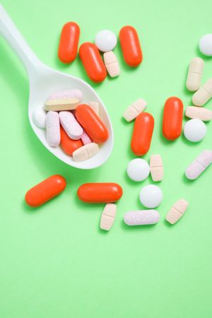 Top view of plastic spoon with pills and vitamins on green table, vertical composition