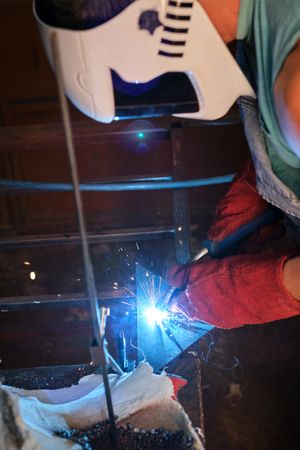 Unrecognizable artisan working on metal in welding workshop