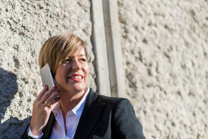 Smiling female in blazer talking on smartphone outside on sunny day