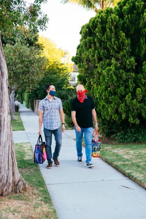 Two neighbors walking on sidewalk together with masks carrying grocery bags