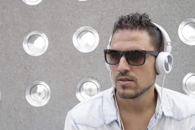 Male listening to something on phone while sitting in front of patterned cement wall