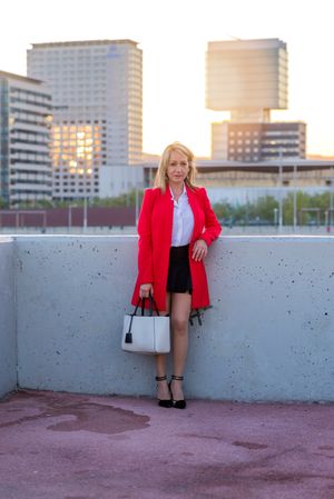 Woman in red coat standing on top of building with view of city behind her