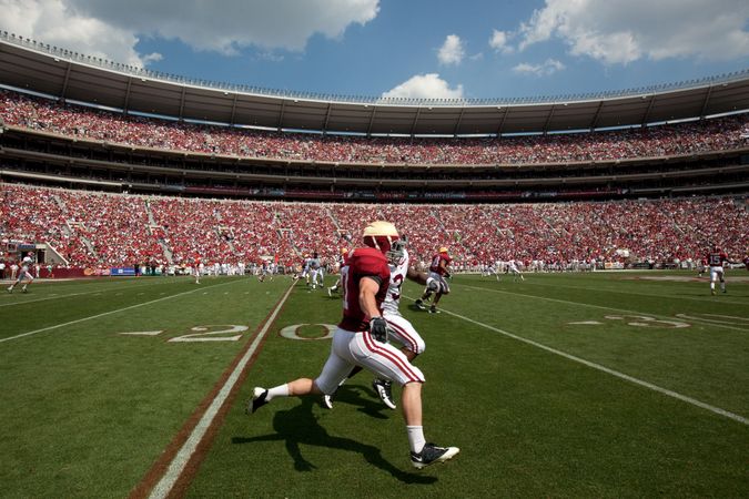 Field view of Alabama Crimson Tide football player during game in crowded stadium