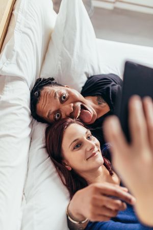 Top view of multiracial couple lying together on bed and taking selfie