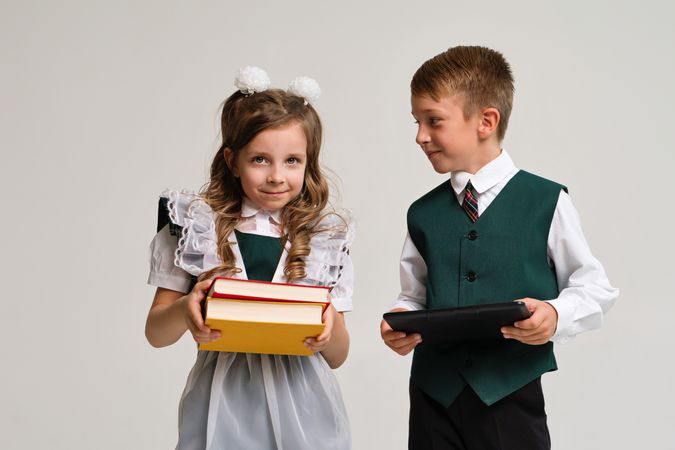 Portrait two elementary school students in uniform with books and tablet pc