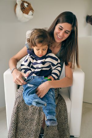 Happy mother putting jeans on son