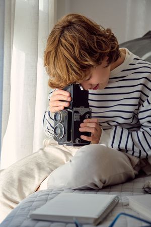 Boy with aged photo camera on bed at home