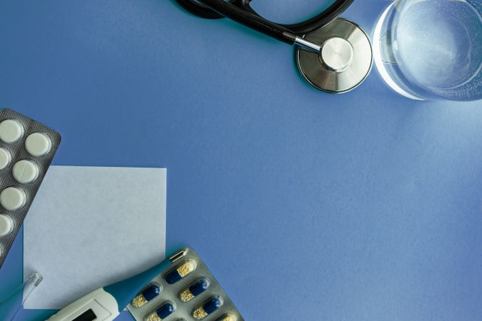 Top view of pills and thermometer with blank note on blue table