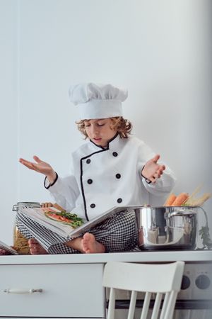 Puzzled preteen boy reading recipe of dish in cook book