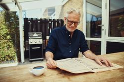 Mature man reading the paper outside with a coffee