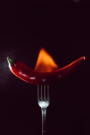 red chili pepper on fire in fork on a dark background