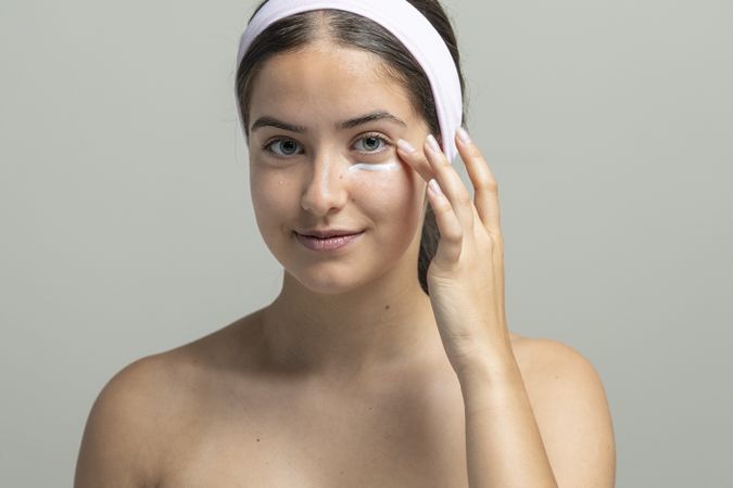 Beautiful woman looking at camera and applying anti-aging eye cream for her skincare routine