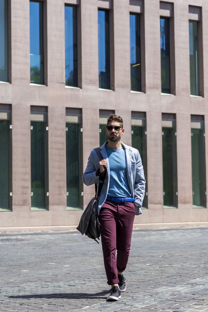 Portrait of a trendy young man walking while holding a shoulder bag