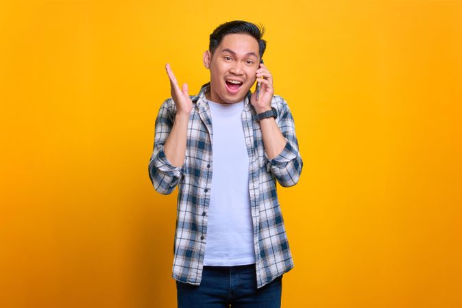 Excited Asian male talking on phone in studio shoot with his hand up
