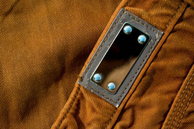 Blank shiny metallic label on bright brown jeans, fabric texture mockup