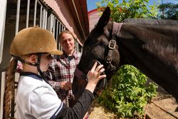 Child engages with horse's face, closely observed by adult