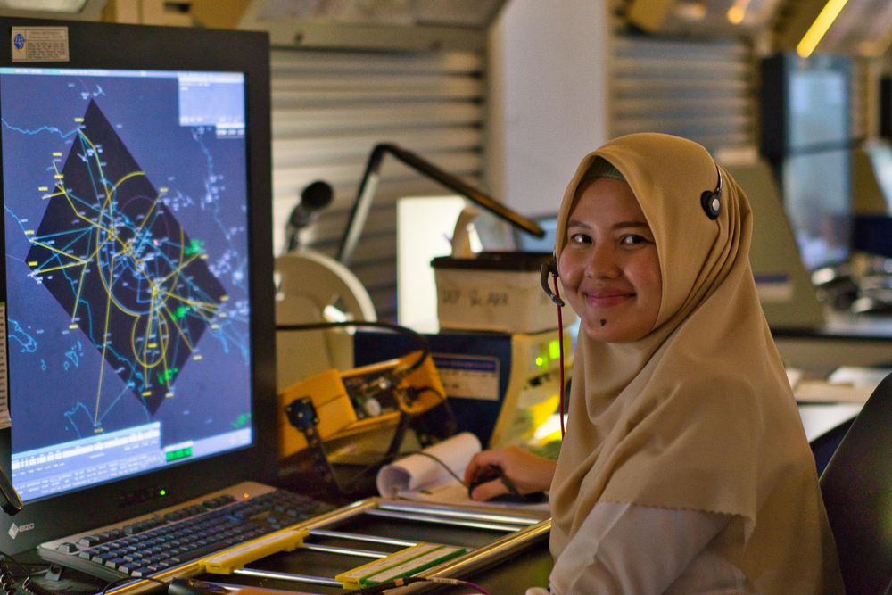 Woman in brown hijab sitting beside flat screen computer monitor