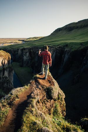 Back of man overlooking edge of cliff taking photo