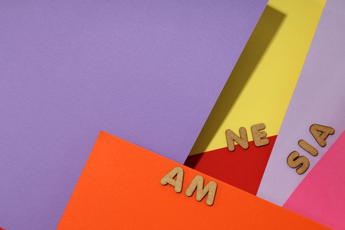 Scattered brown letters spelling “amnesia” on colorful paper background