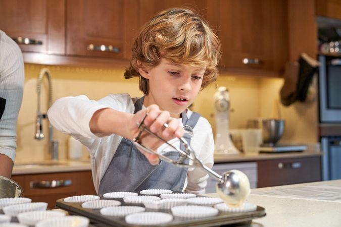 Cute boy filling cupcake baking tray