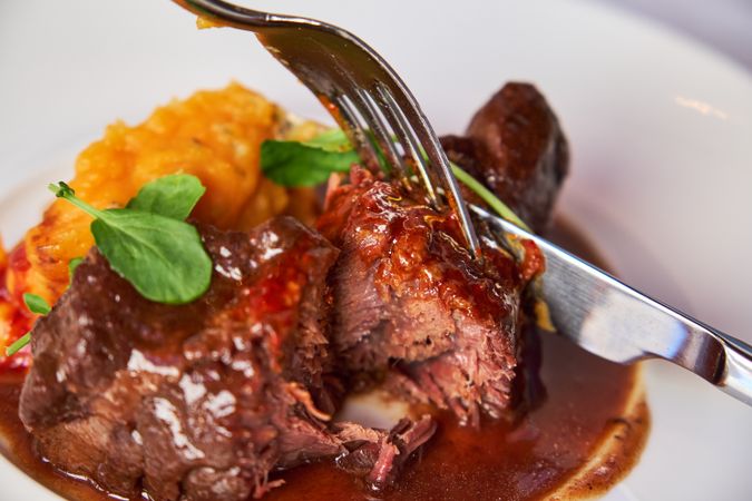 Forks cutting a piece of meat from a dish of veal cheeks with tu