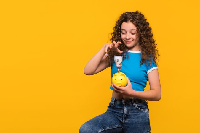 Girl smiling saves money in piggy bank, demonstrating financial responsibility.