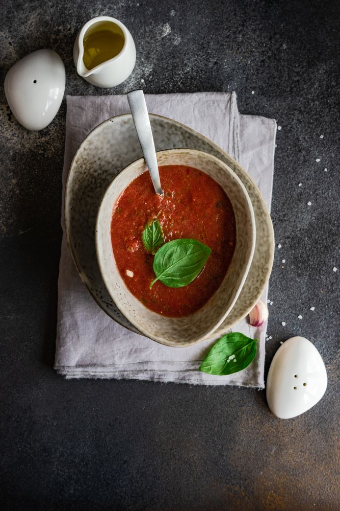 Top view of traditional Spanish gazpacho with basil leaf garnish in grey ceramic bowl