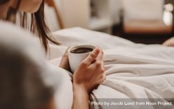 Close up of a woman sitting on bed holding a cup of coffee 0g77e0