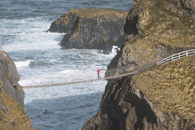 Tourist walking on rope bridge suspended between cliffs in Northern Ireland