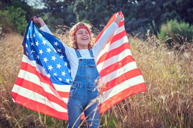 Positive child with flag of USA enjoying sunlight in countryside