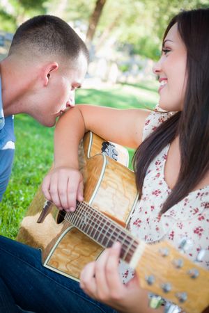 Young Adult Playing Guitar with Partner In The Park.