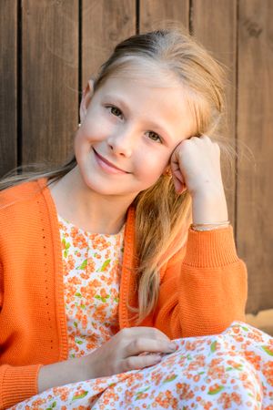 Smiling girl leaning on hand against wooden wall