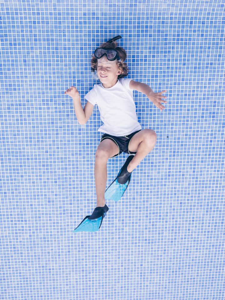 Excited preteen boy on bottom of empty pool imagining swimming