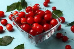 Bowl with red cherry on blue background, close up