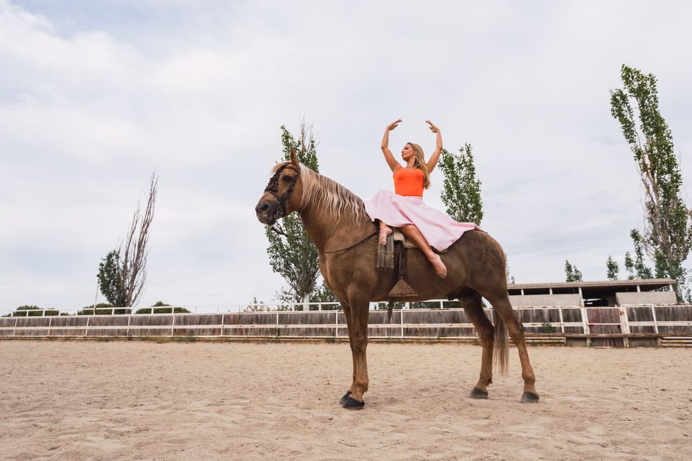 Graceful rider sitting at harnessed horse walking along paddock