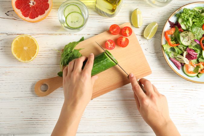 Young woman slices cucumber for salad on wooden background, top view