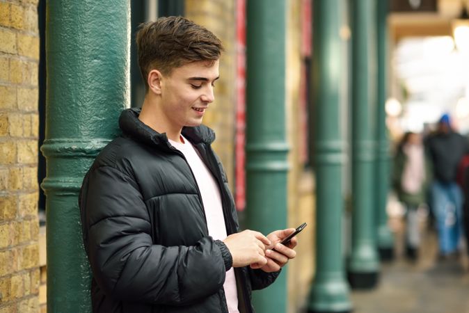 Man smiling while looking down and texting in London street