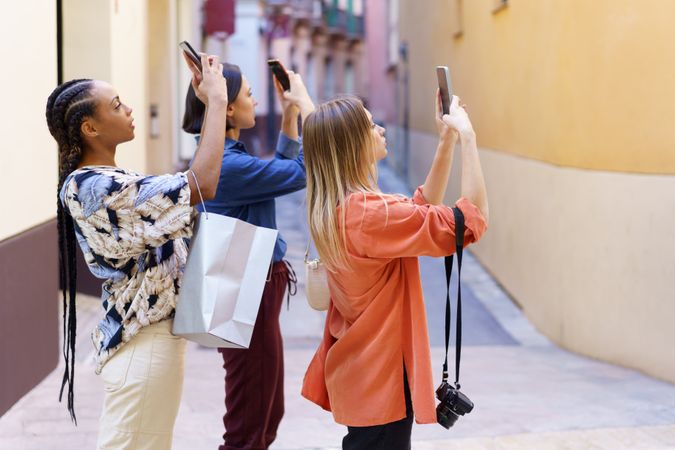 Three women in narrow lane taking pictures with their phone