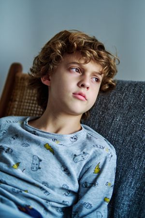 Pensive boy with curly hair sitting on sofa