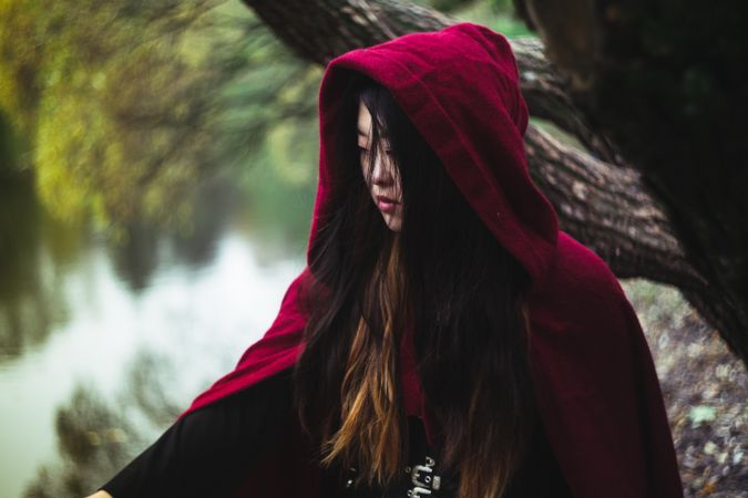 Young woman in red cloak standing beside tree