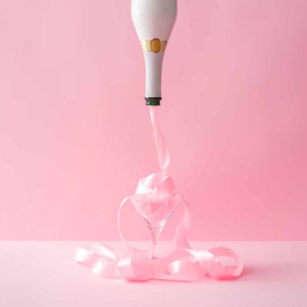Champagne bottle with pink party ribbon on pink background