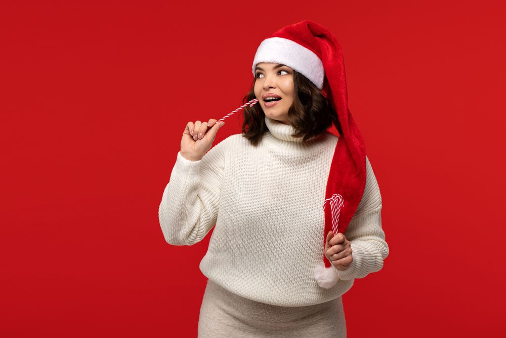 Woman in Santa hat holding festive candy canes near face.