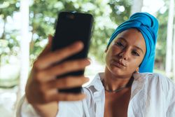 Positive woman with turban on head taking selfie on sunny street