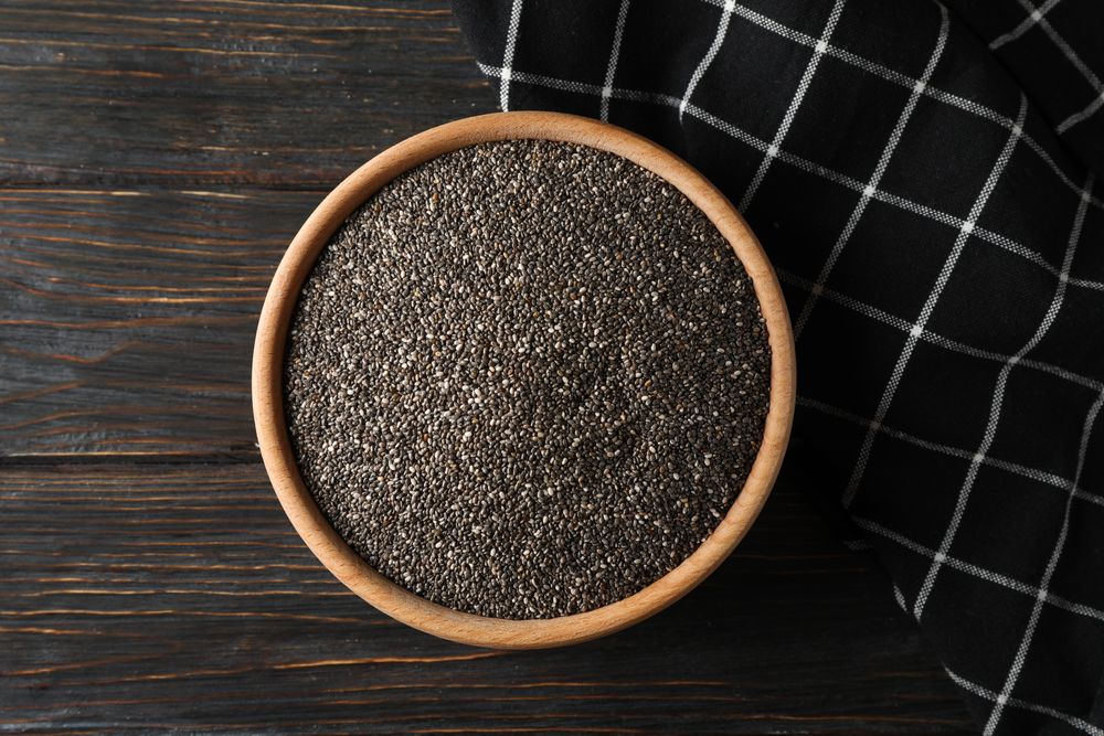 Chia in wooden bowl on wood background, top view