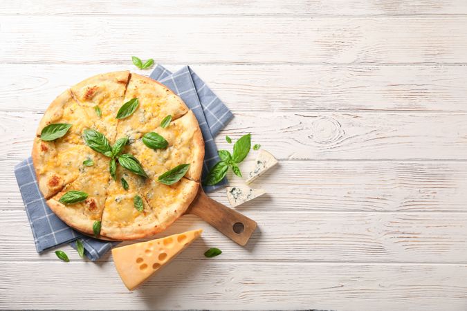 Towel, board, cheese pizza with basil on wooden background, copy space