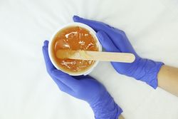 Female hands holding liquid yellow paste for sugaring on blank background, top view